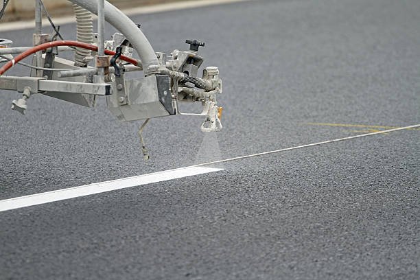 Pavement lane marker machine spraying a white stripe on a new asphalt road. Shallow dof with focus on spray head.